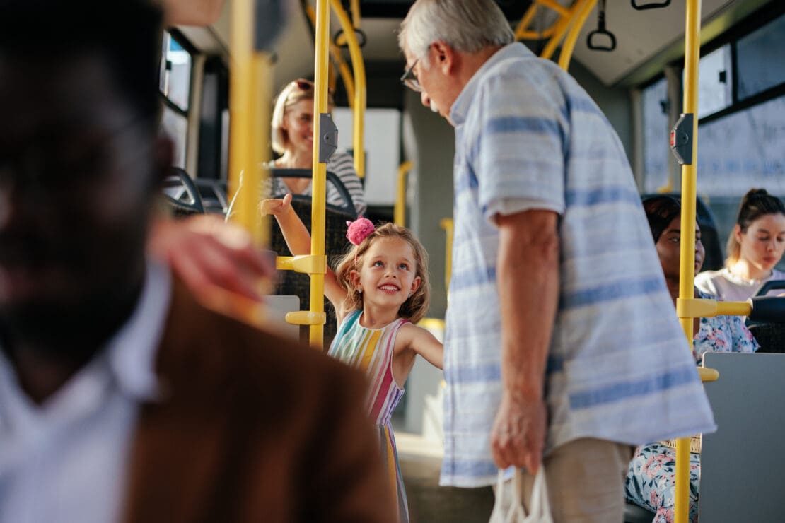 A smiling girl in a colorful dress interacts with an older man on a bustling bus.
